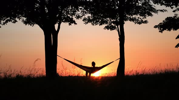 People on vacation. A girl's silhouette in a hammock between trees.