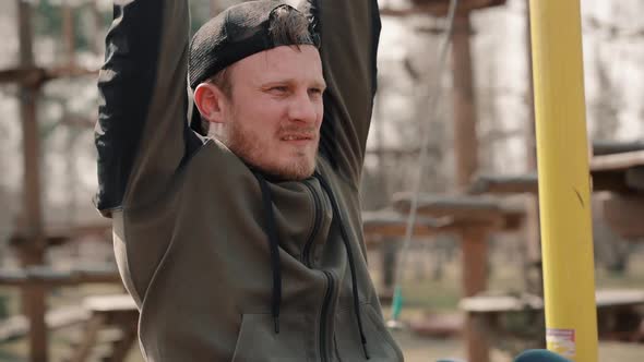 Young Bearded Man Is Doing Exercise on Horizontal Bar on Spring Day in Park.