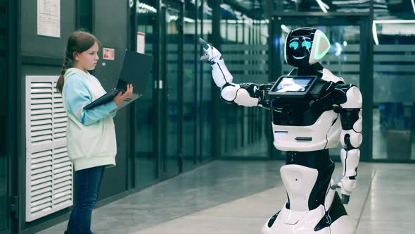 Young Girl Is Operating a Robotlike Machine with a Laptop