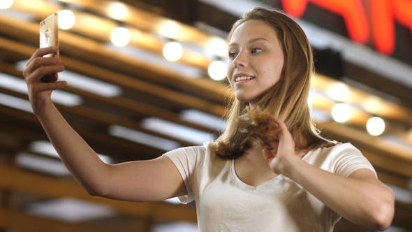 Beautiful woman brushing her hair using a smart phone as a mirror