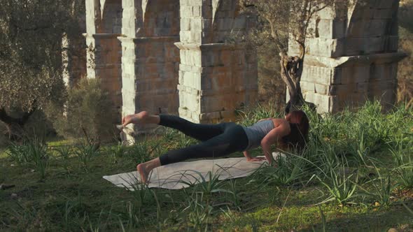 fit female athlete performing Cobra yoga pose exercise within nature at Ancient aqueduct