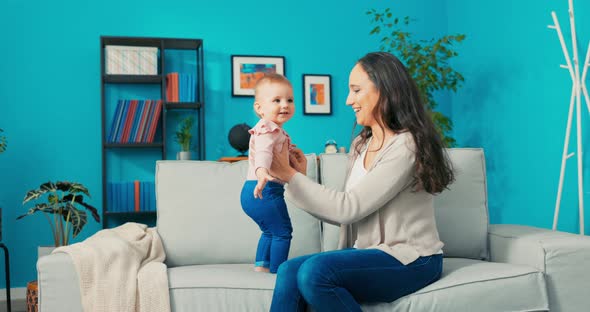 Little Girl with Big Beautiful Eyes Sweet Baby is Standing on Sofa Next to Mom