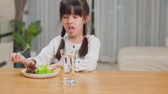 Unhappy Asian little young girl child don't want to eat green vegetables on dinner plate.