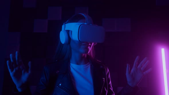 Creative Woman in Futuristic VR Headset Gesturing with Hand While Interacting with Cyberspace Under