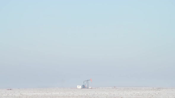 Oil Pumpjack Operating in a Snowy Field on a Foggy Morning