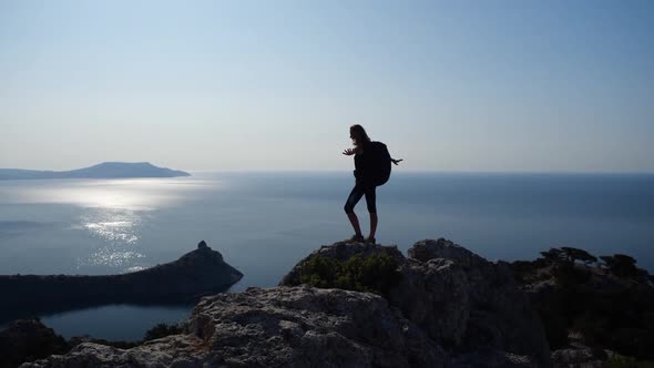 Woman Stands at the Peak of a Cliff and Enjoys the View of the Sea and the Brightest Sun, Spreading