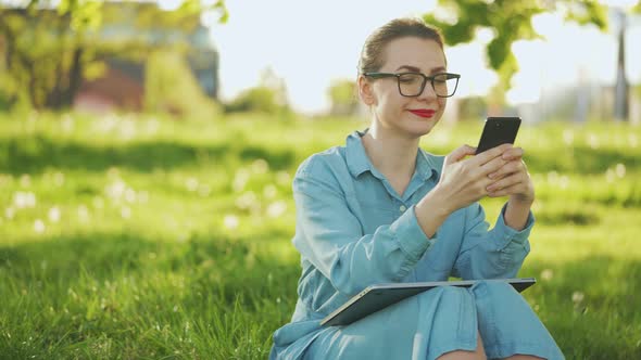 Woman Using Smartphone While Sitting in Park After Finishing Outdoor Work at Sunset