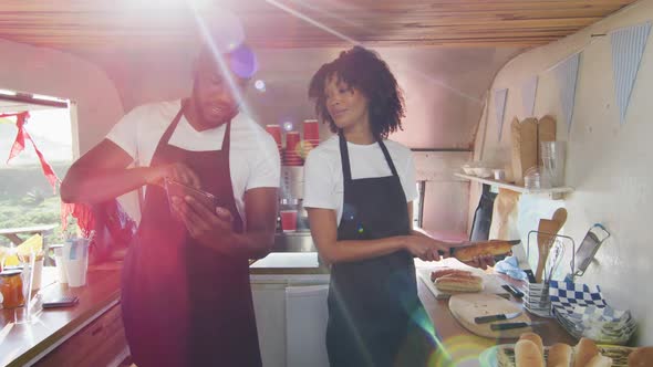 African american couple wearing aprons using digital tablet and preparing hot dogs in the food truck