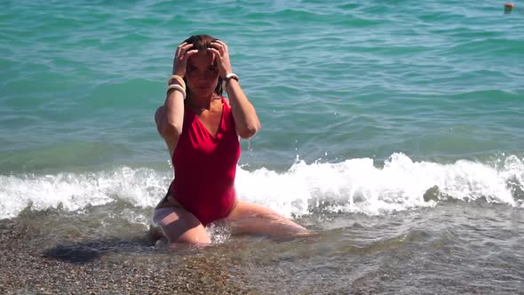 Young Woman with Long Hair in a Red Swimsuit and Bracelets in Boho Style Enjoying the Waves on the