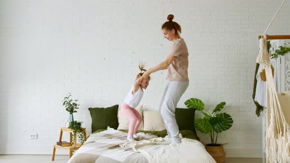 Young Mom and Child Little Daughter Jumping on the Bed