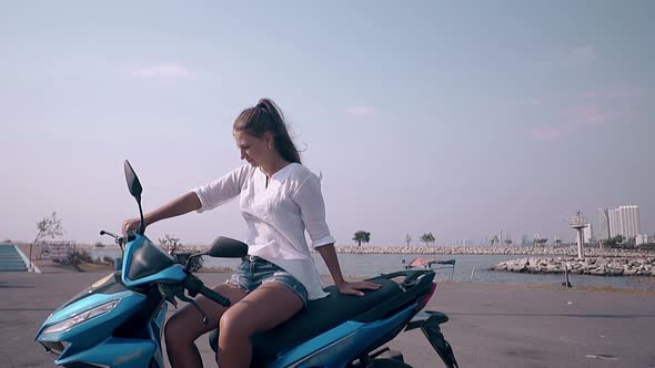 Young Woman with Long Hair Sits on Black and Blue Scooter