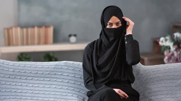 Mystery Arabic Woman Hiding Face Under Niqab Relaxing on Couch at Comfortable Living Room