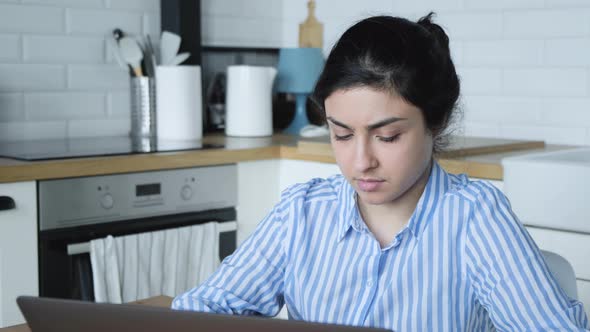 A serious Young Indian girl in a blue striped shirt is working on a computer at home 