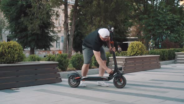 Slow motion of man in white cap riding electric scooter in city