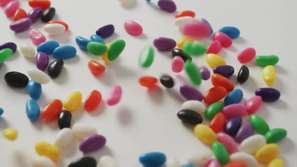 Video of close up of multi coloured sweets falling over white background