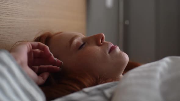 Closeup Side View of of Cute Young Woman Waking Up and Opening Eyes While Lying in Comfortable Bed