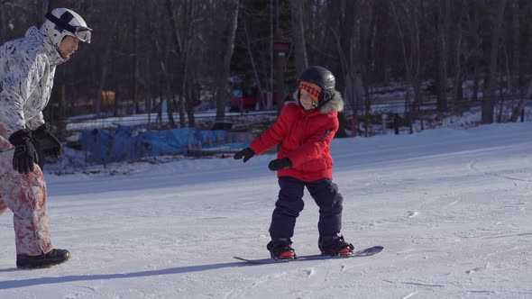 Young Man Snowboard Instructor Tiches Little Boy How To Ride a Snowboard. Winter Activities Concept