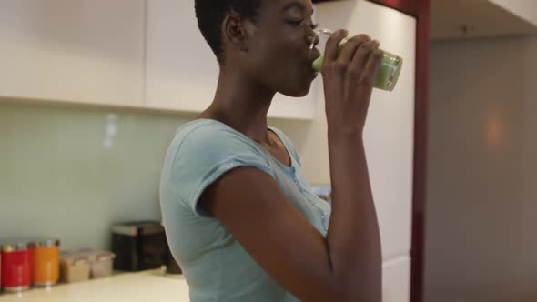 Profile of smiling african american attractive woman drinking homemade smoothie in kitchen