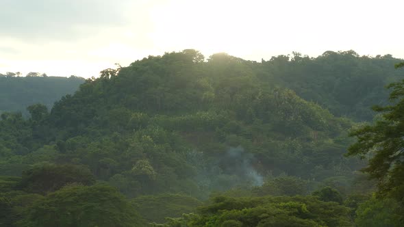 Beautiful scenery landscape of the rainforest hills with the sun setting above and smoke coming from