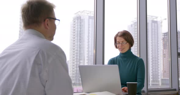 Business consultation of a friendly woman looking into a laptop and a male client in the office.