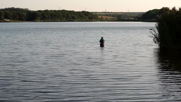 Fisherman Stands with a Fishing Rod in the Water