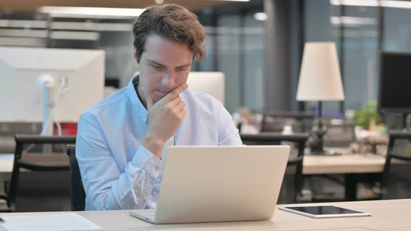 Man Thinking While Working on Laptop in Office