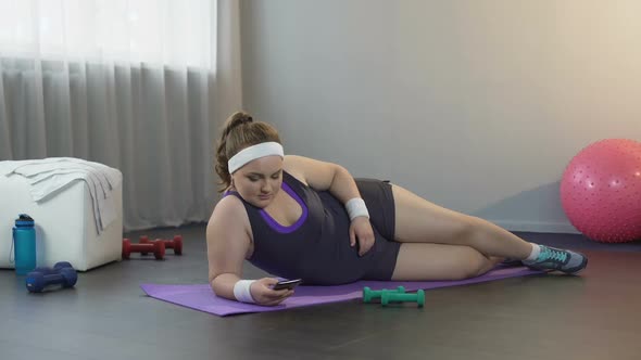 Lazy Fat Girl Lying on Mat, Scrolling Social Media on Gadget Instead of Workout