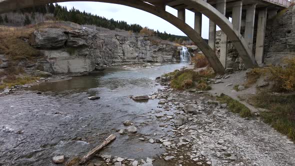 Slo-Mo aerial shot approaching Lundbreck falls while flying underneath an arch bridge in southern Al