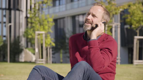 A Middleaged Handsome Caucasian Man Talks on a Smartphone with a Smile As He Sits in a Street