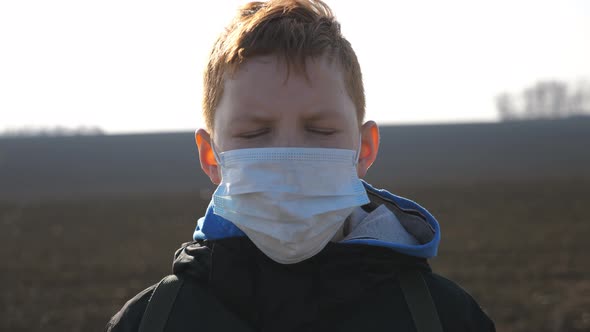 Portrait of Little Boy with Medical Face Mask Standing Outdoor. Sad Male Child Wearing Protective