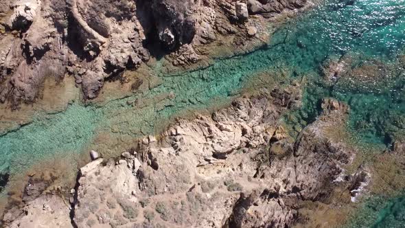 Drone soars over a rock in the middle of the sandy beach of Chia in Sardinia's south, stunning weath