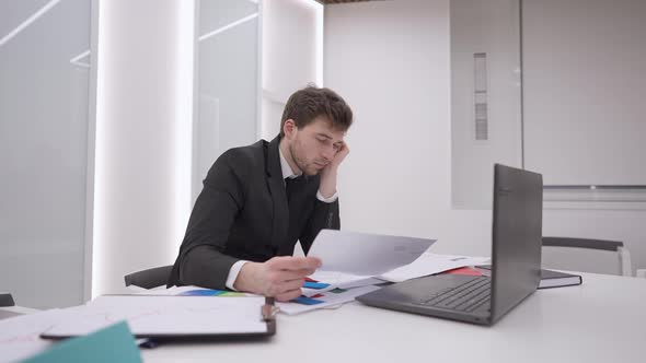 Exhausted Tired Caucasian Man in Suit Falling Asleep at Table in Office Indoors