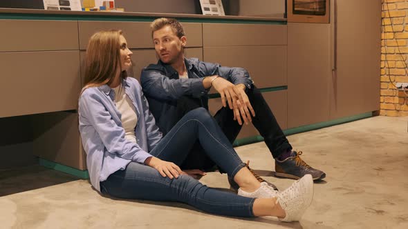 A Young Couple Is Sitting on the Floor in a Kitchen Showroom, They Look Tired and Depressed