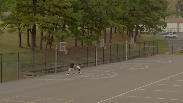 two teen boys play one on one basketball on an outdoor court