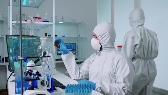 Scientist in Ppe Suit Holding Petri Dish While Studying Virus Samples