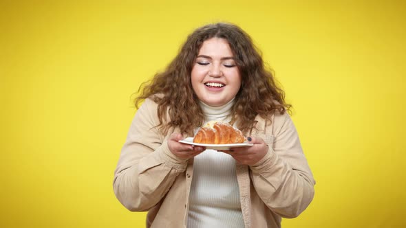 Overweight Young Woman Smelling Delicious Sweet Croissant Smiling Looking at Camera