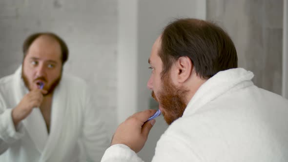 Young Man with Toothbrush Cleaning Teeth and Looking Mirror in Bathroom