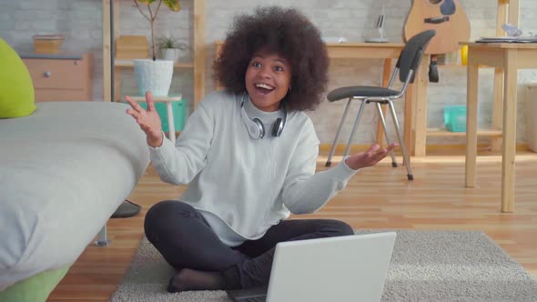 Beautiful African American Woman with an Afro Hairstyle Sitting on the Floor with a Laptop Learned