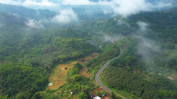 4K Aerial view from a drone flying above rural clouds, road in a tropical forest in Thailand