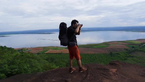 man traveler with backpack using camera taking a photo on the edge of cliff