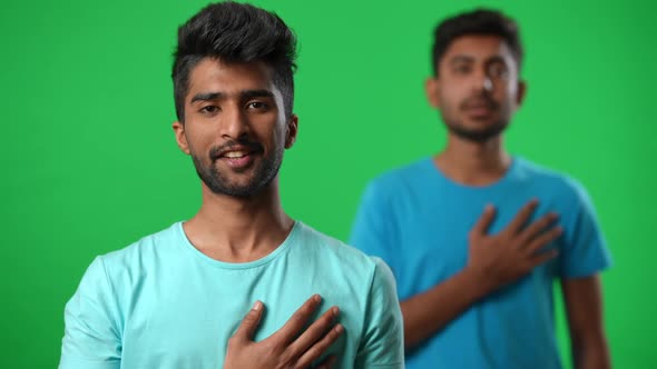 Positive Handsome Middle Eastern Man Singing Anthem Holding Hand on Chest with Blurred Friend at