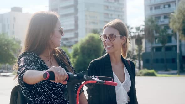 Talking woman pushing electric scooter, walking by friend in city