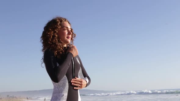 A young woman surfer putting on wetsuit.