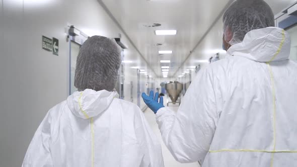 Two Scientists Talking and Wearing Protective Suit Walking Through Manufacture Hallway