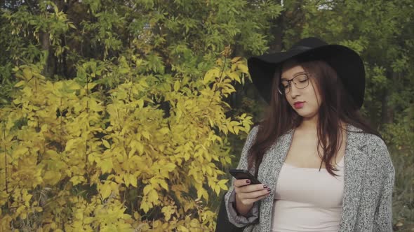 Young Pretty Woman in Black Hat and Glasses Typing Sms to Her Boyfriend Outdoor