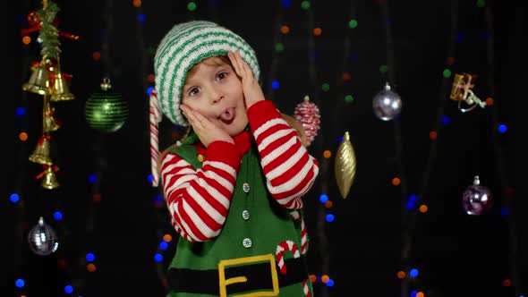 Kid Girl in Christmas Elf Santa Claus Helper Costume Cover Face with Hands and Plays Hide and Seek