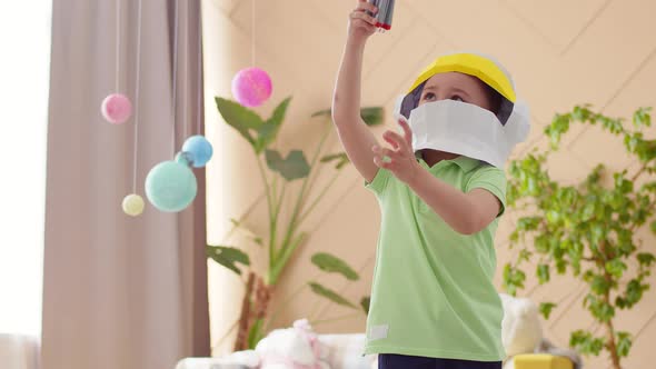 Boy is playing with rocket, turning it over in air among planets on strings, in the nursery. alt