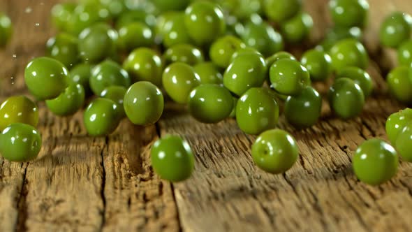Super Slow Motion Shot of Rolling Fresh Green Olives on Old Wooden Table at 1000 Fps.