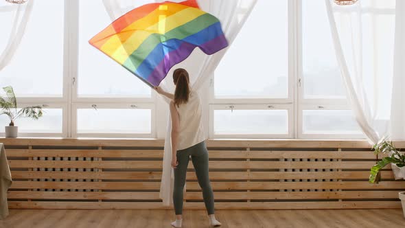 Female Holding LGBT Gay Flag in Hands and Waving on Sunset in Sunny Rays