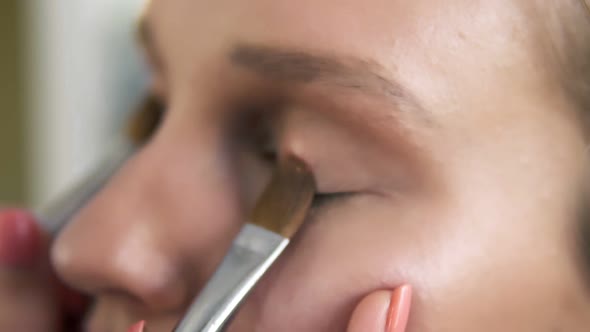 The Makeup Artist Puts Light Shiny Eyeshadow on a Model's Eyelids Using Two Professional Brushes